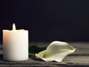 Burning candle and white calla on dark background with copy space. Sympathy card